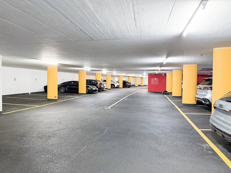 Indoor parking garage with multiple levels, concrete floor, yellow support columns, and parked cars.