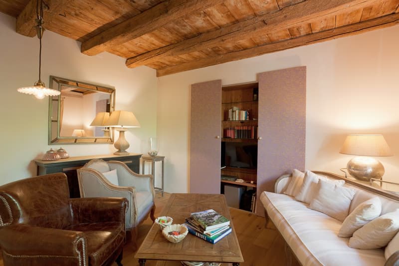 Cozy living room with wooden beamed ceiling, leather armchair, wooden coffee table, bookshelf, and lamps