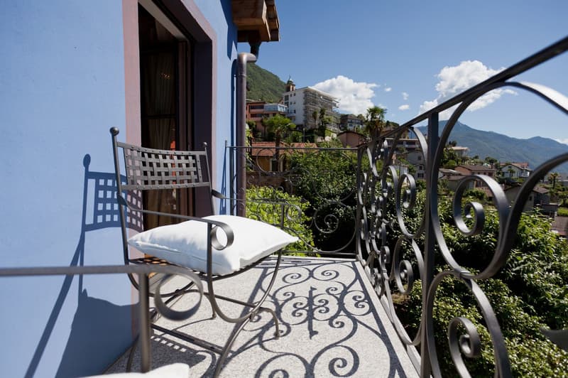Balcony with wrought iron railing, wicker chair, and view of buildings and mountains in the background