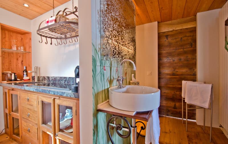 Rustic kitchen with wooden cabinets, granite countertop, hanging pot rack, vessel sink on wooden vanity, and decorative wall mural