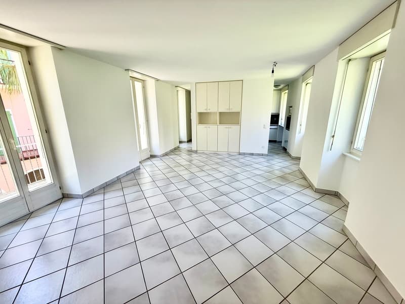 large room, white tiled flooring, white walls, double doors leading to balcony, built-in cabinets, windows, tiled hallway, hallway with white walls, power outlet