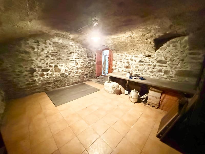 Room with stone walls, wooden floor, small desk, bottle, stone, and lamp.