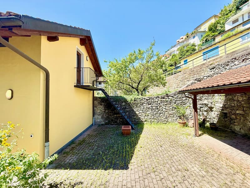 yellow stucco wall, brown roof, brick ground, balcony, outdoor potted plants, small tree, small fence
