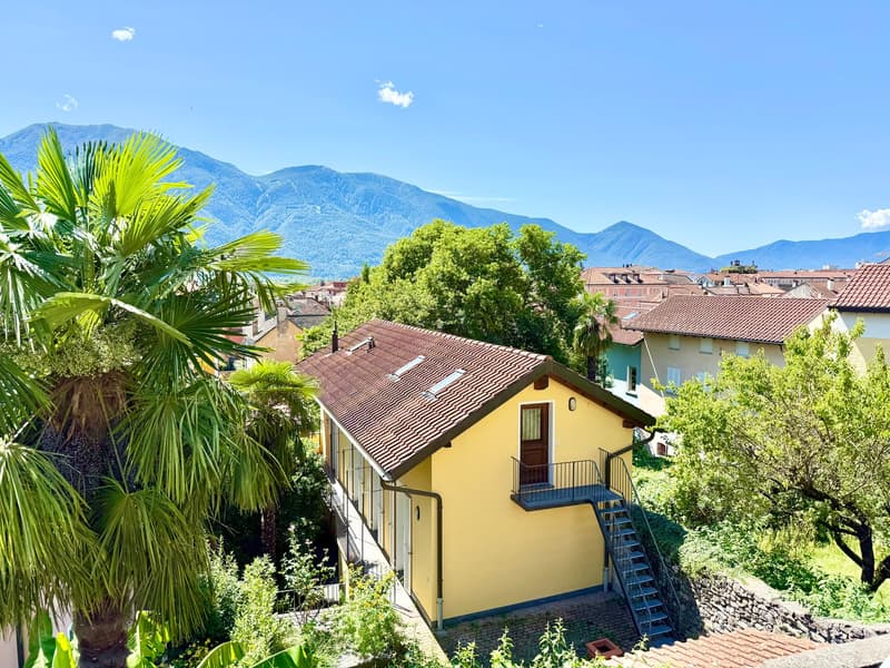 Yellow single-family house, brown tiled roof, chimney, entrance, metal staircase leading to balcony, garden, palm trees, mountains in the background