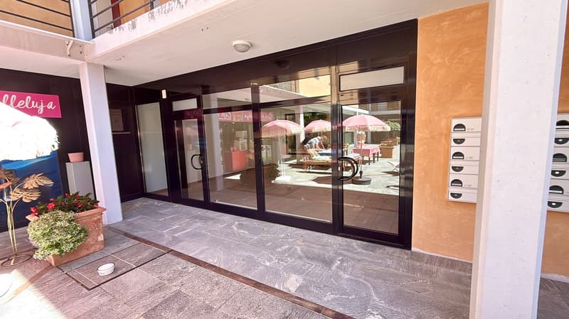 Main entrance of a residential building, large sliding doors, plants, open balcony, outdoor seating area with umbrellas