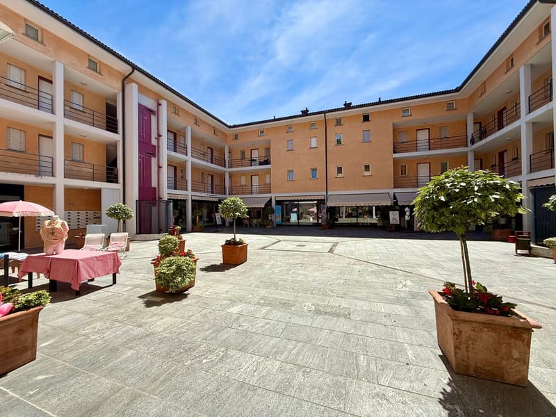 A courtyard surrounded by an apartment building with balconies, greenery, and a table under an umbrella.