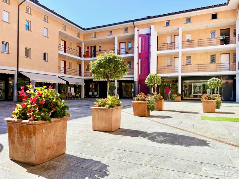 Modern apartment complex with multiple floors and a courtyard area with large planters and a pathway.