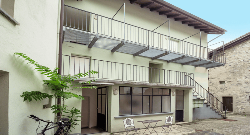 Two story house with metal railings on the balconies, glass windows, a door and a bicycle parked to the left side of the entrance