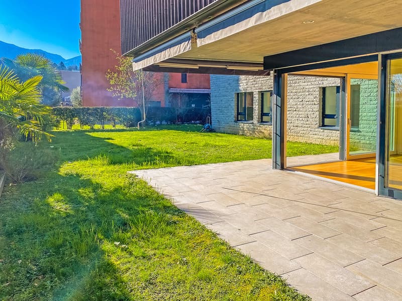 A well-maintained garden with a paved walkway leading to a covered terrace with glass doors.