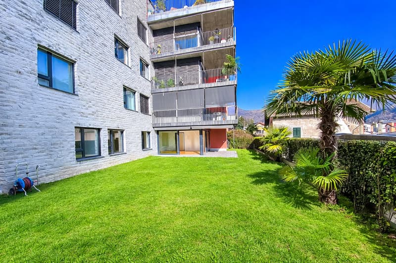 Modern apartment building with balconies, white brick facade, green lawn, palm trees