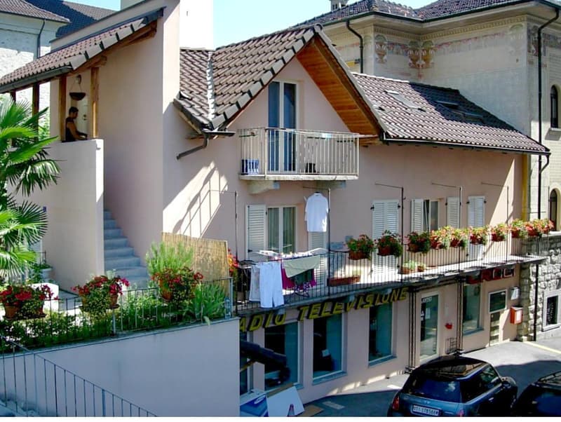 two-story house, tiled roof, several balconies, exterior steps, potted plants, cars parked in front
