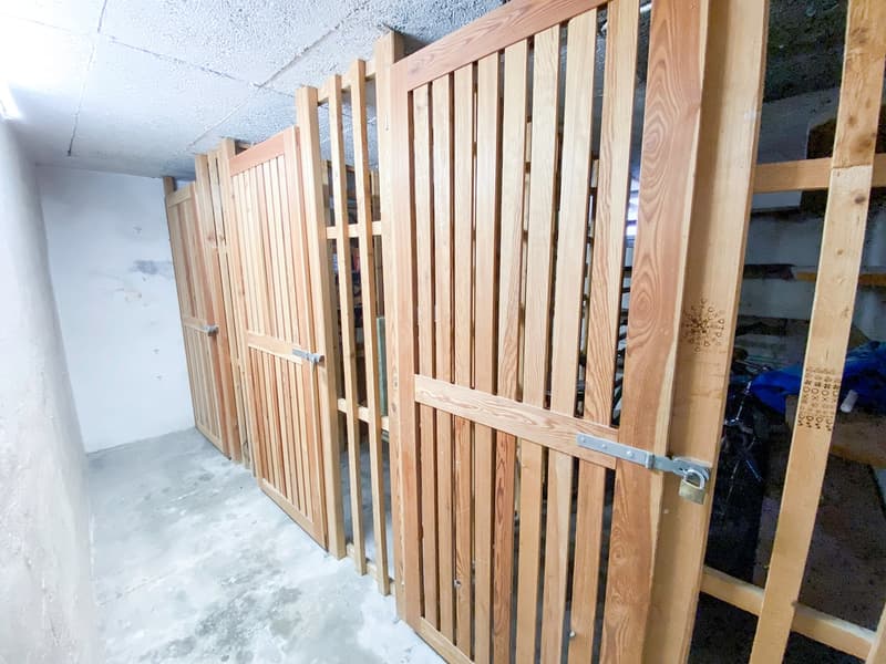 Row of wooden storage lockers, two with padlocks, concrete floor, white walls, light ceiling