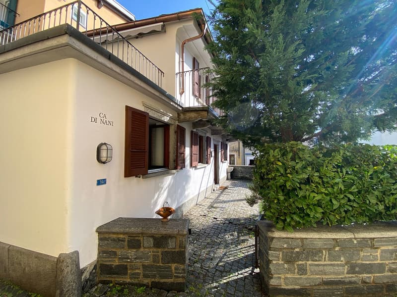 White-painted building, balcony on upper floor, brown shutters, cobblestoned alleyway