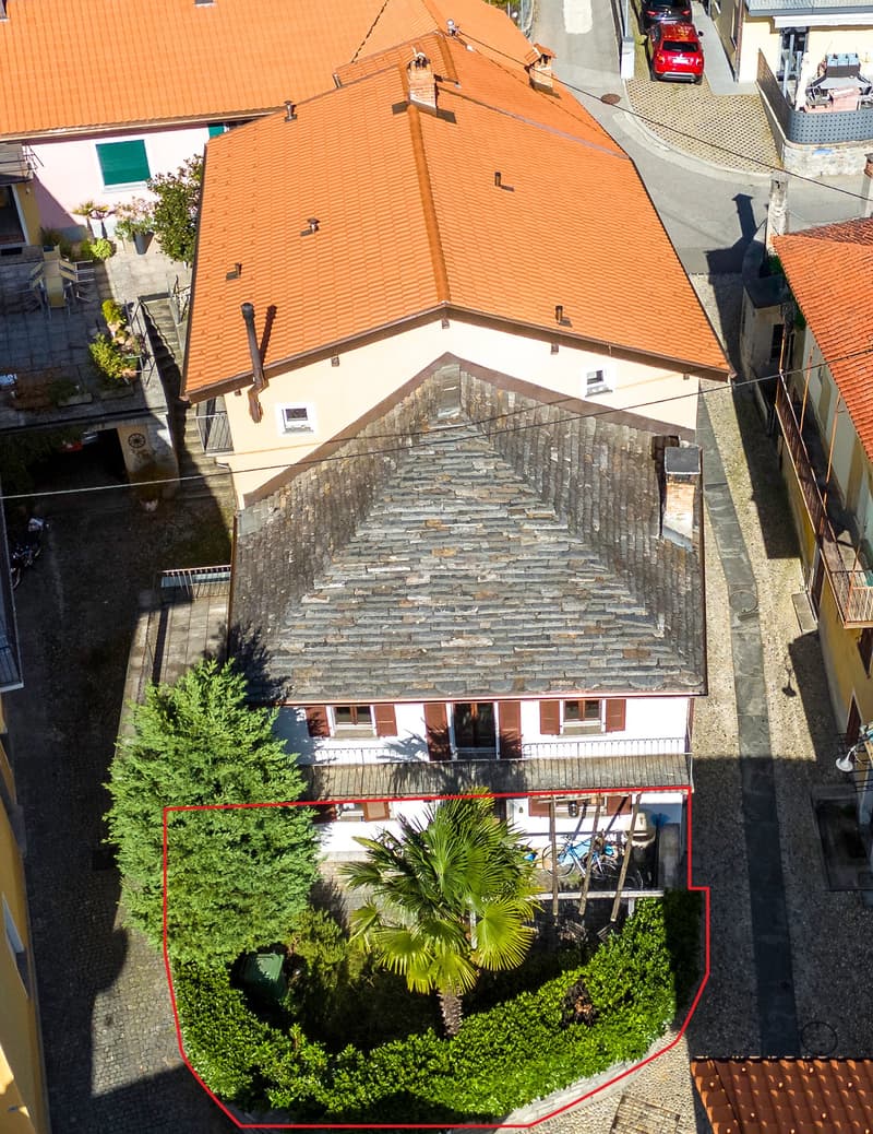 Two-story house, red roof, surrounded by bushes, located on a raised ground floor