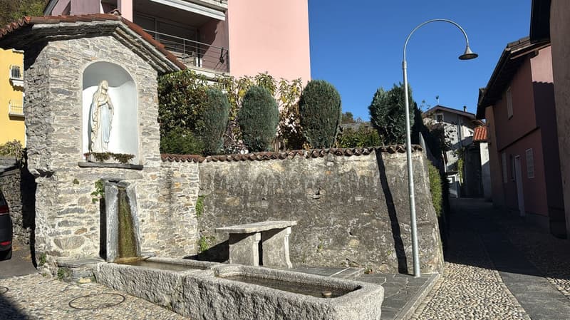 stone house facade with small wall fountain, pink building in background