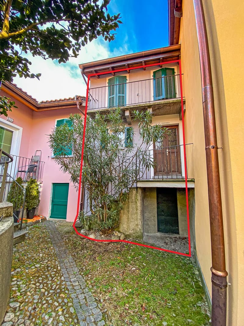 House with terracotta roof, beige wall, entrance at ground level, balcony on first floor with iron railings, a tree in the middle of the image, a red square around a small house.