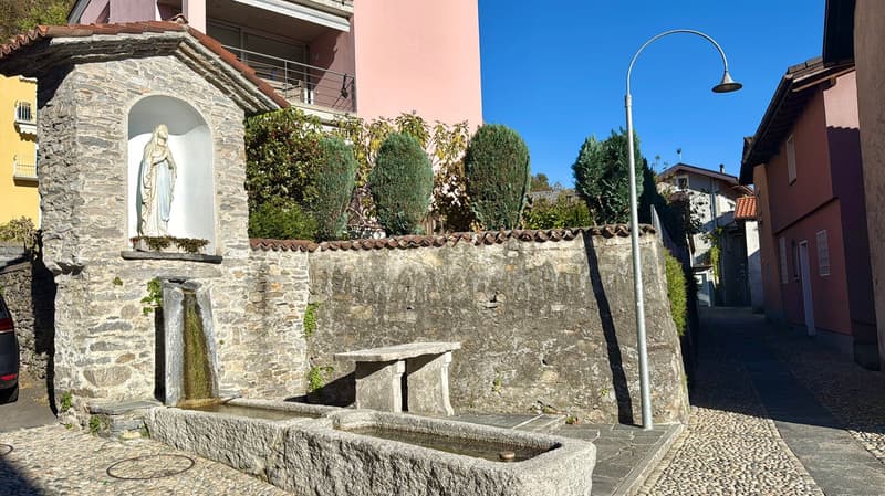 A stone fountain, a stone table, a stone wall, greenery and buildings