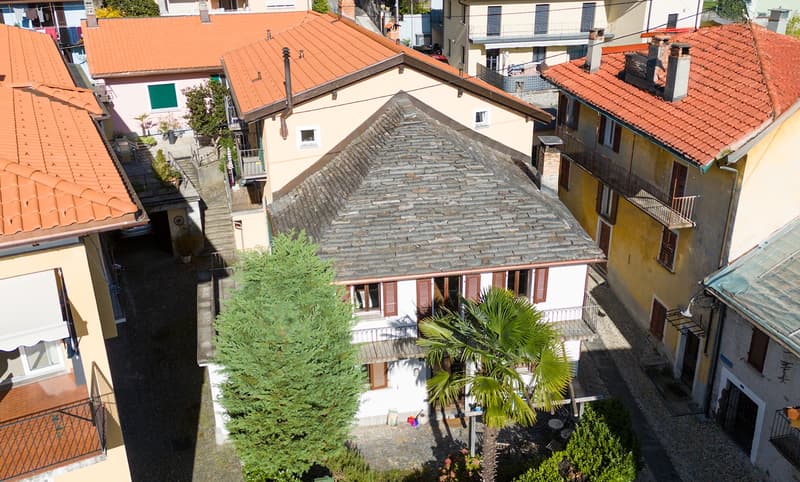 3 story building, white painted, stone roof, balcony on each floor, garden, trees