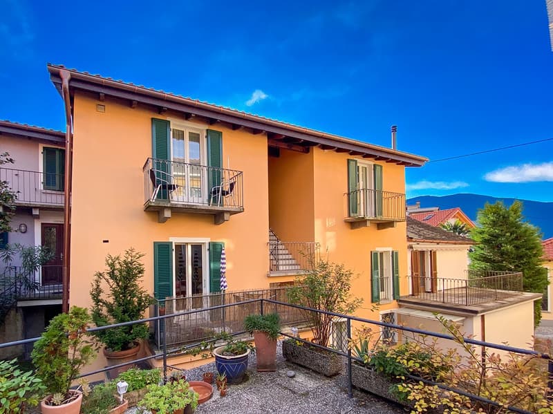 3 story house, yellow color, balcony, terrace, stairs, windows with shutters, garden with plants, mountains in the background