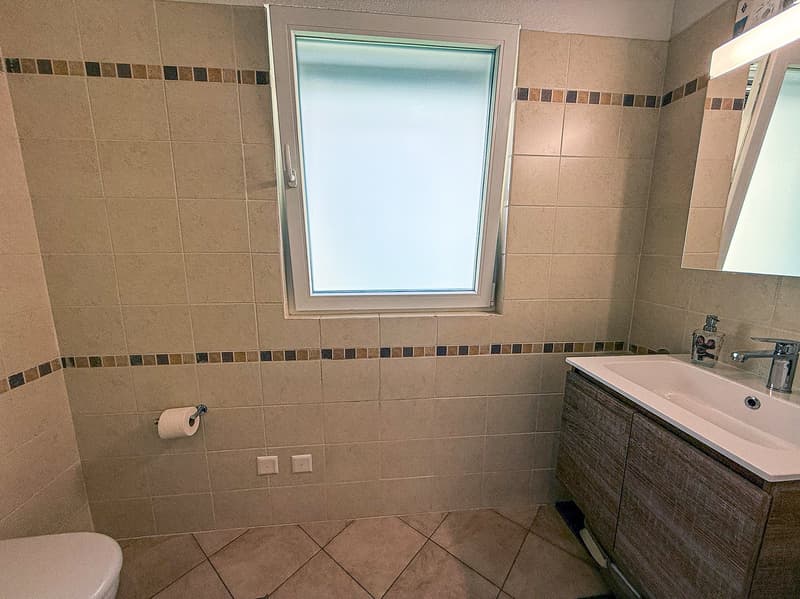 Bathroom with beige tile walls, a window, a vanity with a sink, and a toilet.