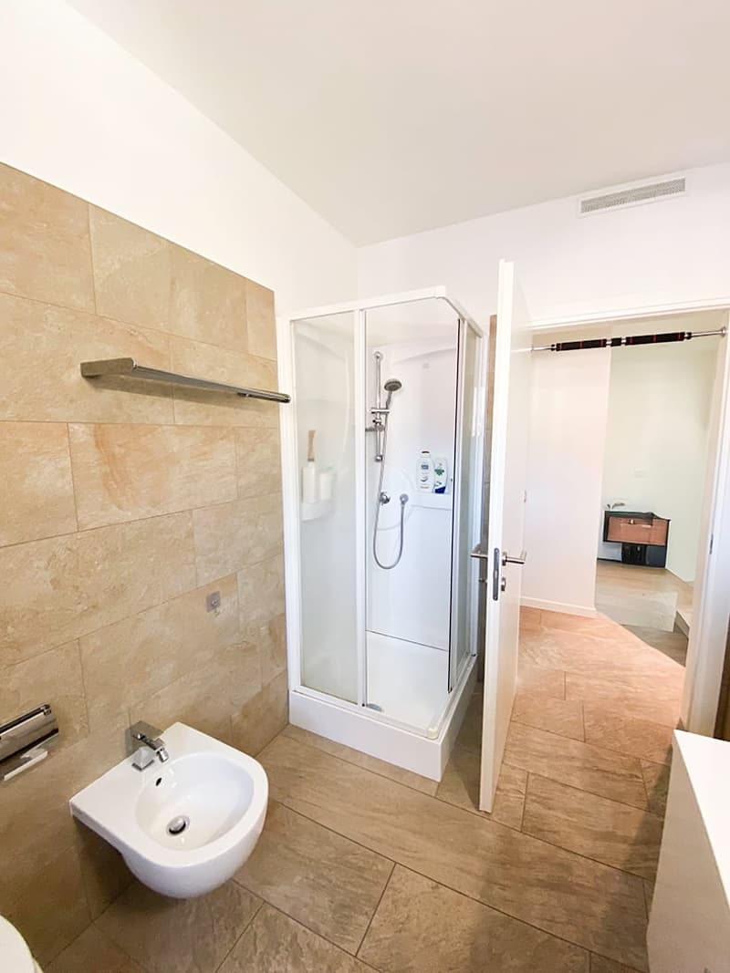 a modern bathroom with a shower, a sink, tiled floors, and a partially open door