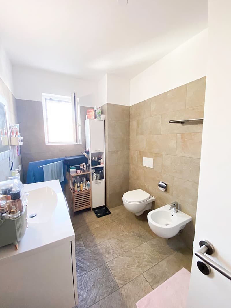 modern bathroom with beige tiled walls and floor, white sink and white toilet bowl, towel rack and bidet