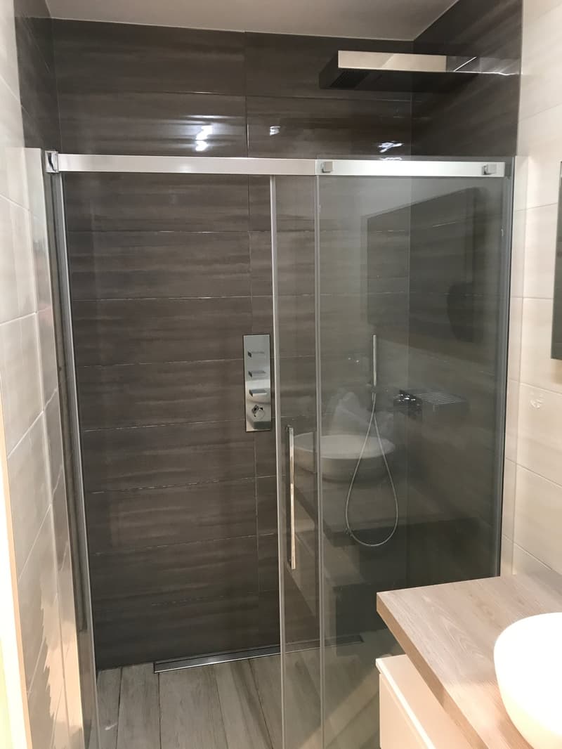 modern shower room with glass door, tiled wall, sink, wooden countertop, white basin, shower head