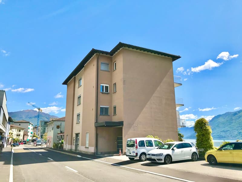 multi-story building, beige walls, multiple windows, cars parked in front, mountains in the background