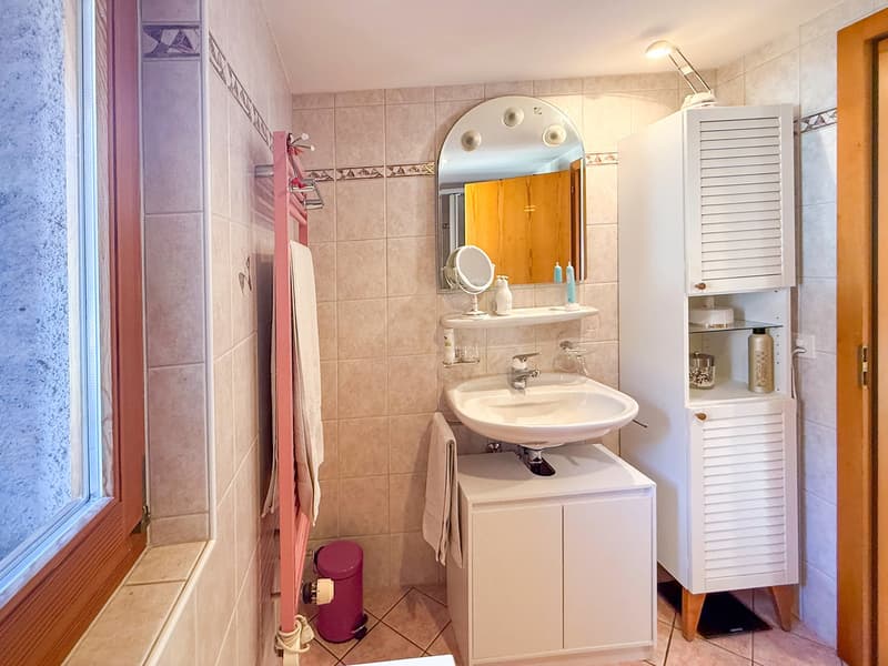 Bathroom with sink, mirror, cabinets, and a window. Tiled floors and walls.