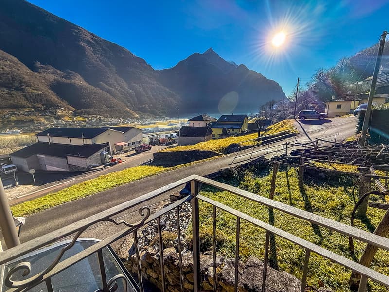 Balcony with railings overlooking a road, a hillside with buildings, mountains in the background, sunny weather