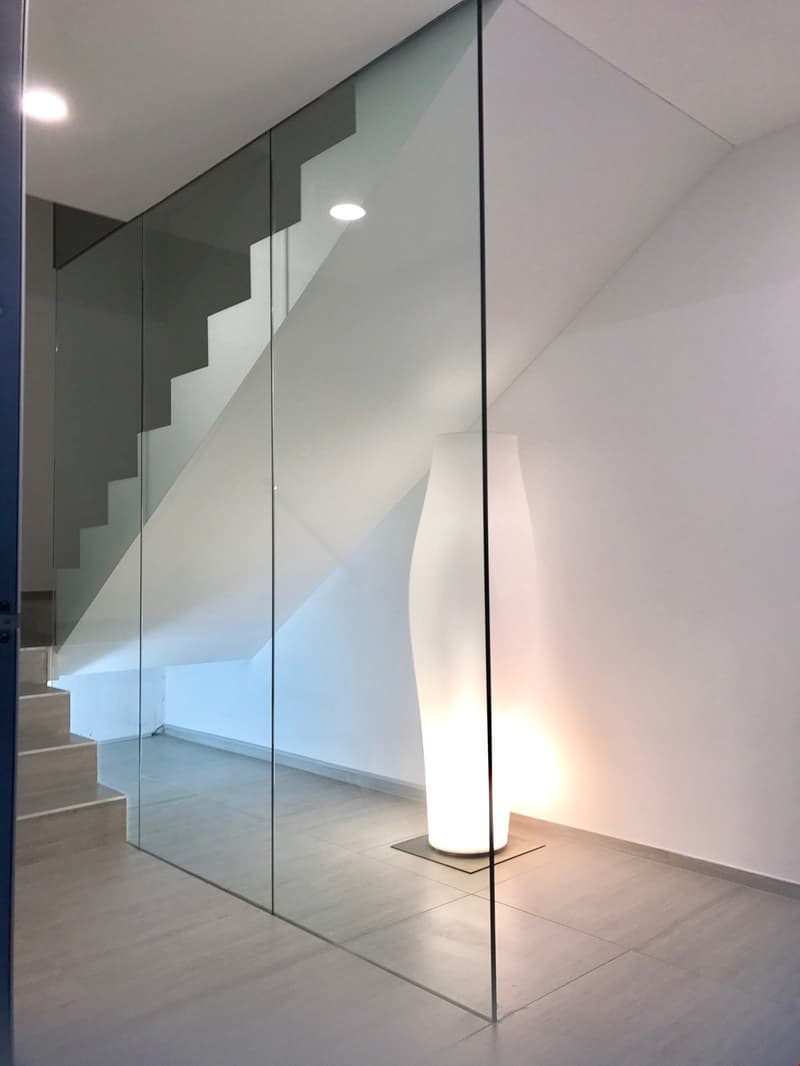 The image shows a modern interior with a glass wall, a white floor lamp, and a staircase visible in the background.