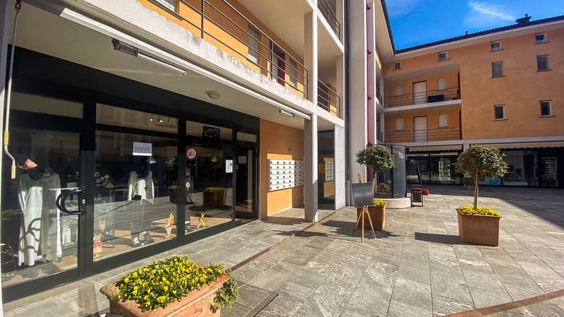 Modern building with balcony, entrance to shop, front yard with planted trees and pavement.