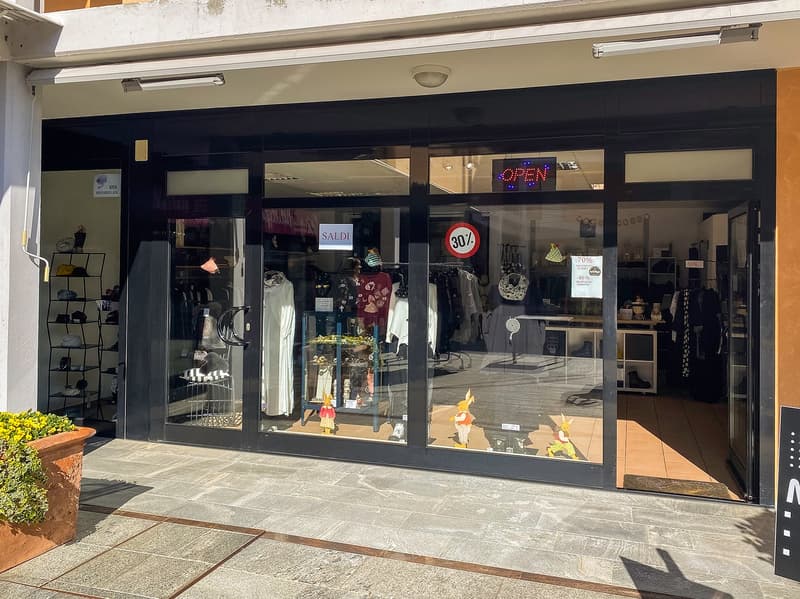 Clothing shop with glass walls, a small flowerbed at the entrance, and a digital sign board that says 'OPEN'