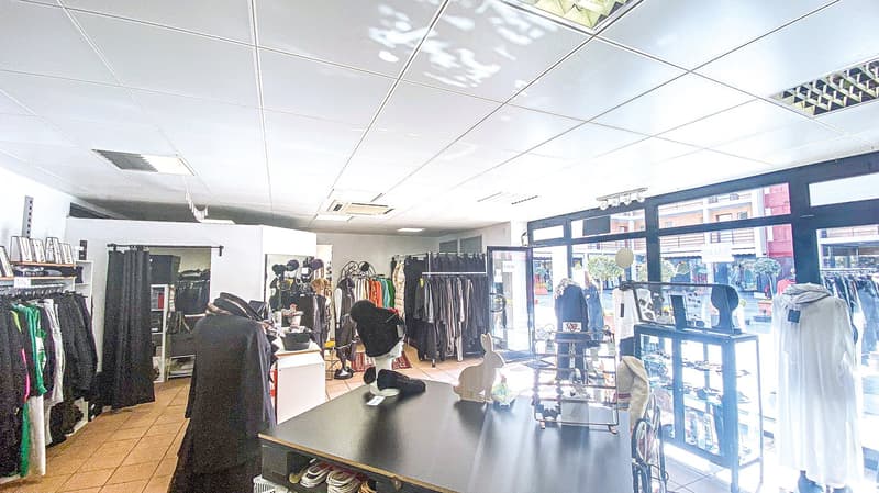 Shop interior with clothing racks, counter with a display, tables with various items, glass walls, wooden flooring.