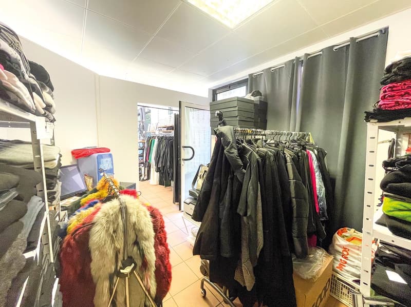 shop interior with clothes on shelves and racks, white walls, white ceiling tiles, open door