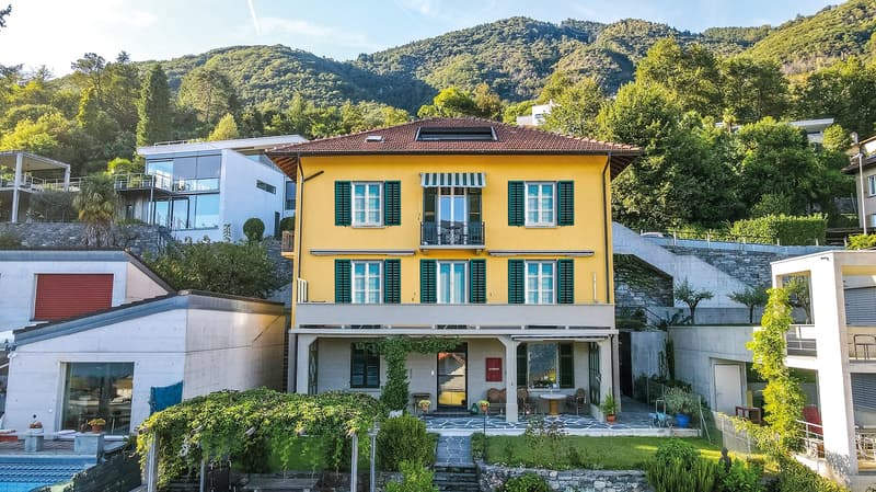 Yellow house, 2 stories, green shutters, large windows, balcony, green bushes, mountain view