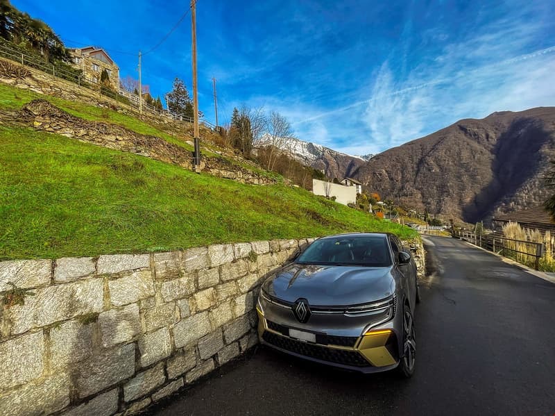 Car parked on side of road with a stone wall, grass on one side, mountain in background.