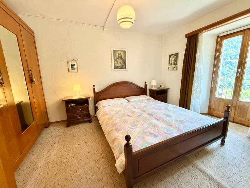 A bedroom with a bed, wooden nightstands, a lamp, a wardrobe, picture frames, a white wall, and carpeted floor.