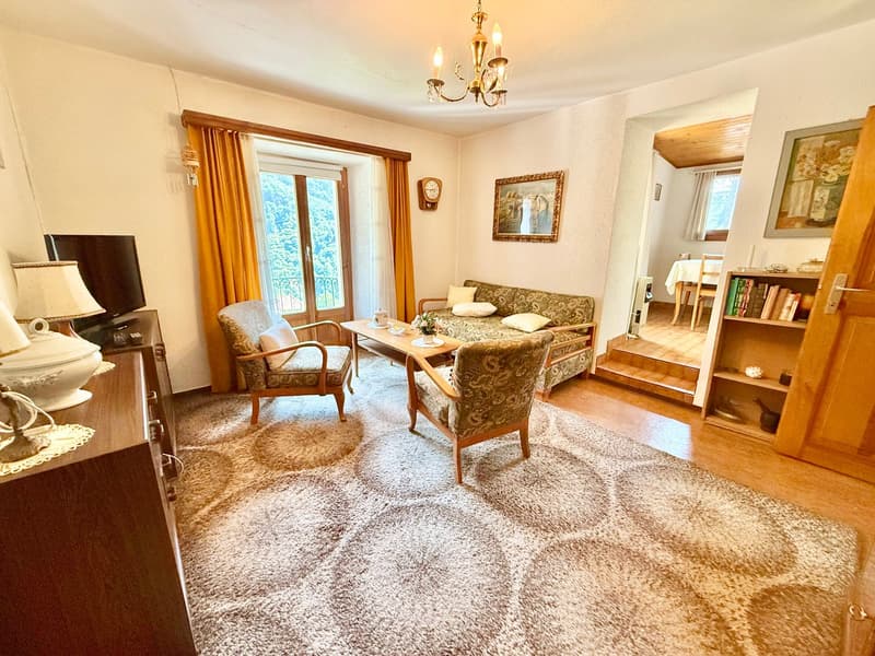 white walls, large rug, a sofa, a center table, chairs, chandelier, lamp, wooden cabinet, tv