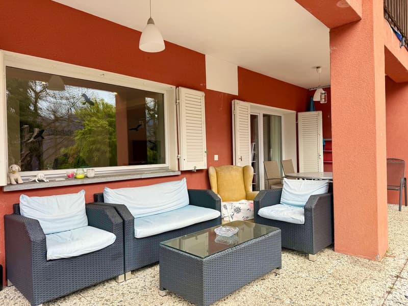 outdoor seating with a glass table, red walls, large window, wicker chairs, a yellow chair, lamps, tables and chairs in the background