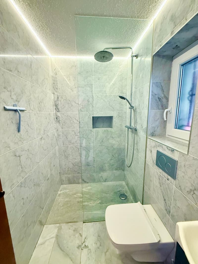 modern bathroom with a glass shower enclosure, a marble wall and floor, a toilet, and a sink