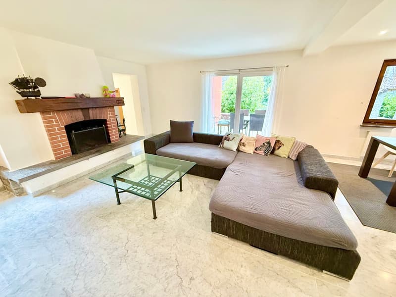 L-shaped sofa with several cushions, glass top coffee table, brick fireplace with a shelf above it, white marble floor