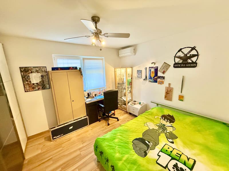 bedroom with a bed, desk with chair, wardrobe, fan, air conditioner, posters, and decorations on the wall
