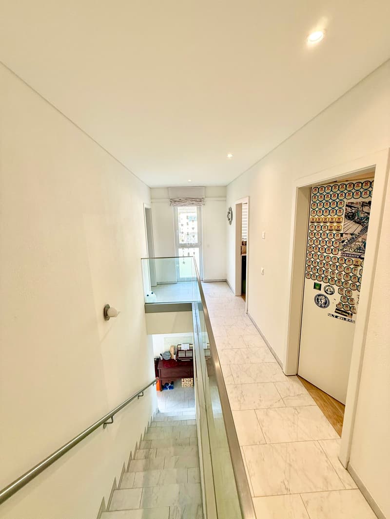 White tiled staircase, glass railing, handrail, wooden interior doors, balcony with railing, wall-mounted light