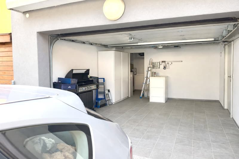 Garage area with ceiling lamps, wall cabinets, white wardrobe, ladder, trolley, storage boxes, griller and car parked