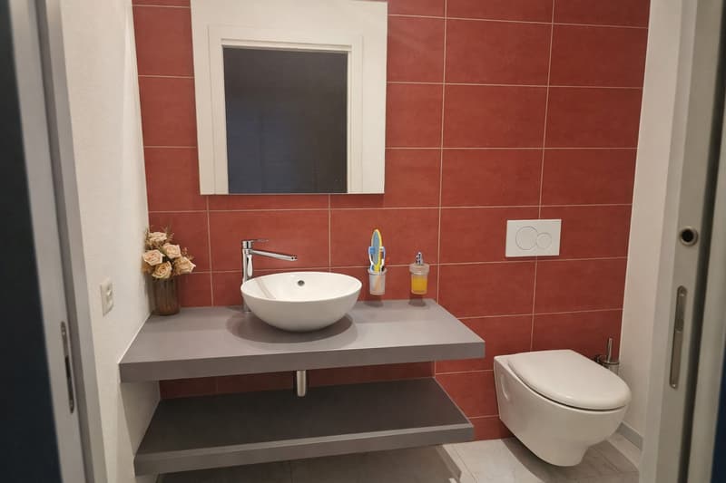 white sink with faucet, white toilet, floating shelves, tiled wall, power outlet, mirror