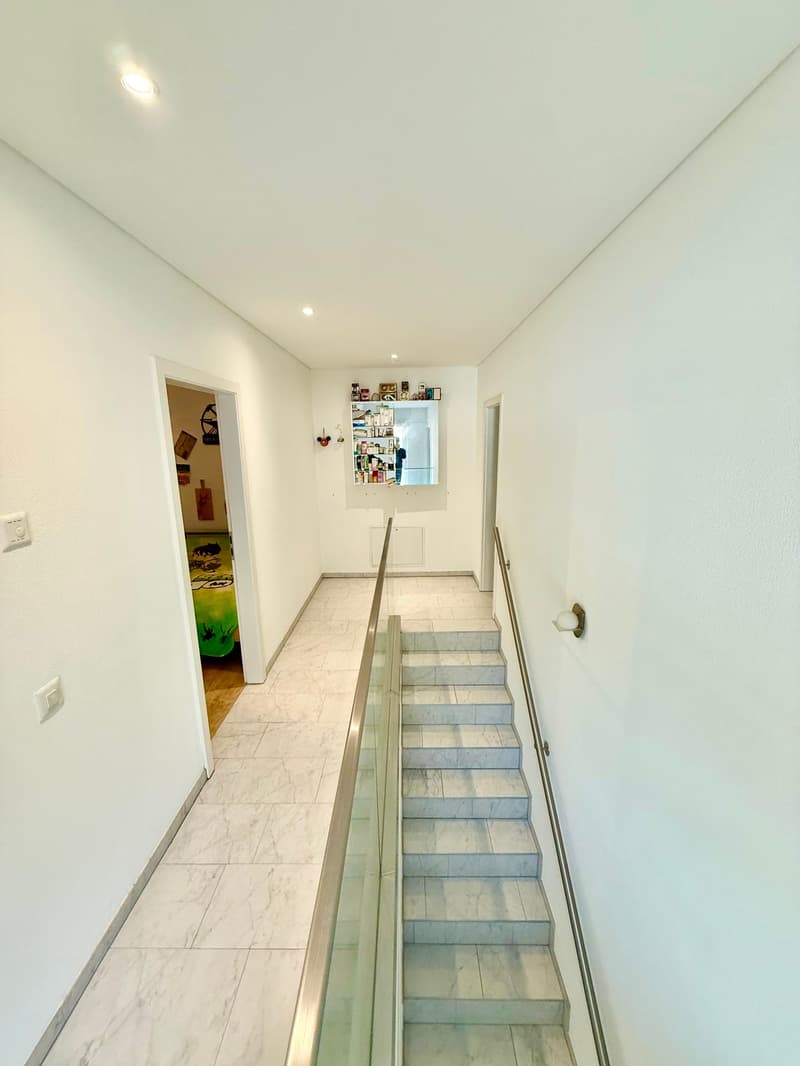 White walls, white tiled floor, railings on stairs, hallway light, hallway
