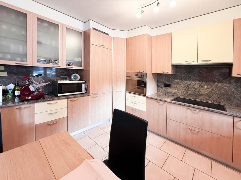 modern kitchen with wooden cabinets, granite countertops, built-in oven and microwave, marble backsplash, tiled floor, black dining chair, marble island, gas stove, and a wine bottle
