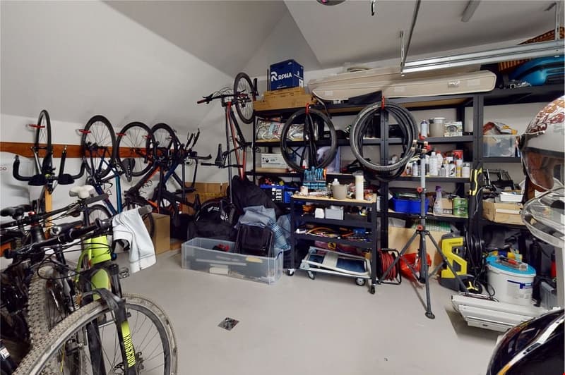 Multiple bicycles on wall, bikes on floor, tools on shelves, foldable table, various equipment