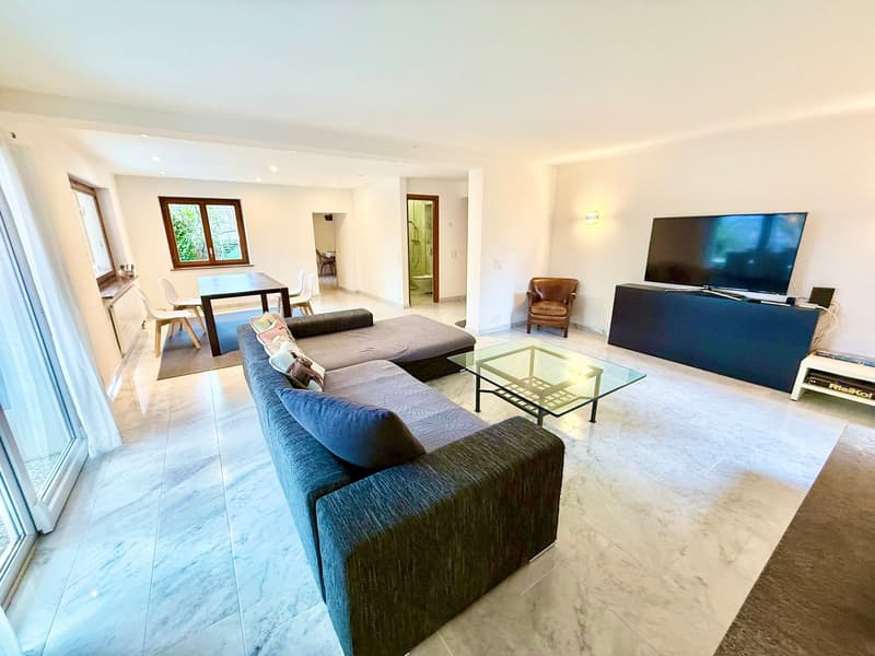 Modern design, large couch, coffee table, flat screen TV, dining area with table and chairs.
